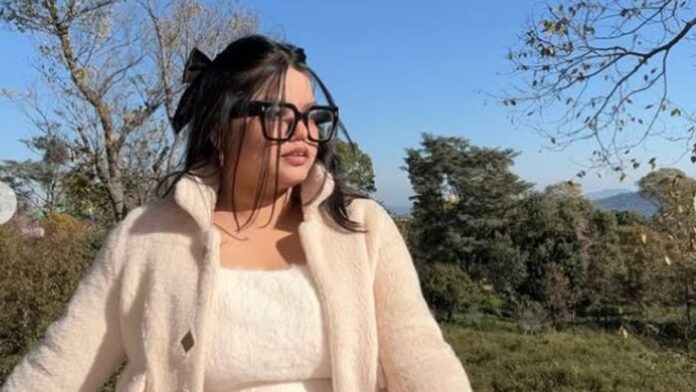 Misha Agrawal in a white winter outfit posing outdoors with trees and blue sky in the background